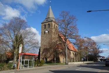 Alsweder Kirche Backsteinkirche mit spitzem Turm und rotem Dach, umgeben von kahlen Bäumen und blauen Himmel.