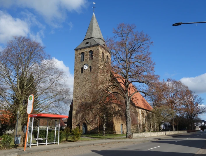 Alsweder Kirche Backsteinkirche mit spitzem Turm und rotem Dach, umgeben von kahlen Bäumen und blauen Himmel.