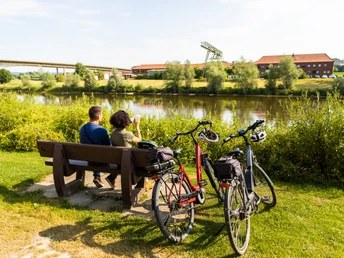 Vlotho-Hafen-Teutoburger-Wald-Tourismus-H-Tornow-014.JPG Ein Paar genießt den Ausblick auf einen Fluss von einer Parkbank; zwei Fahrräder stehen daneben.