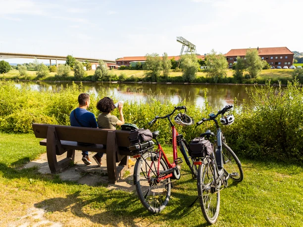 Vlotho-Hafen-Teutoburger-Wald-Tourismus-H-Tornow-014.JPG Ein Paar genießt den Ausblick auf einen Fluss von einer Parkbank; zwei Fahrräder stehen daneben.