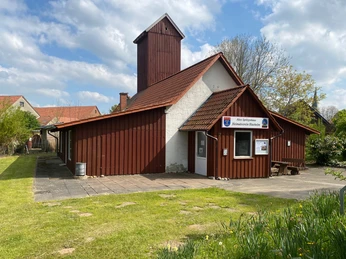 Das historische Blasheim Spritzenhaus aus rotem Holz hat einen markanten Turm und eine Wiese davor.