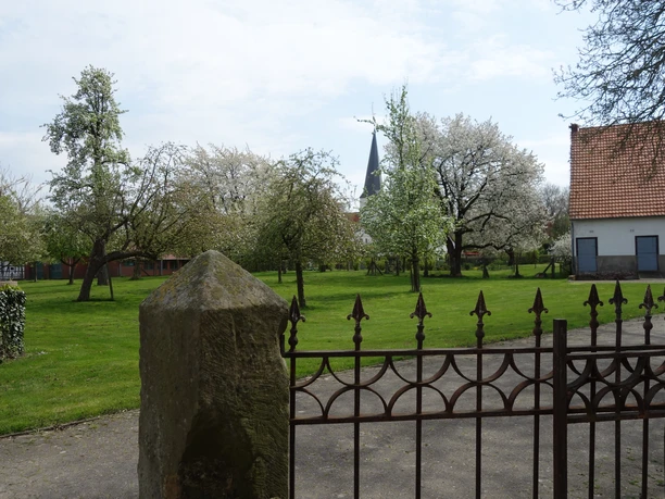Blasheim Ein gepflegter Garten mit Kirschbäumen, einem Zierzaun und im Hintergrund eine Kirchturmspitze.
