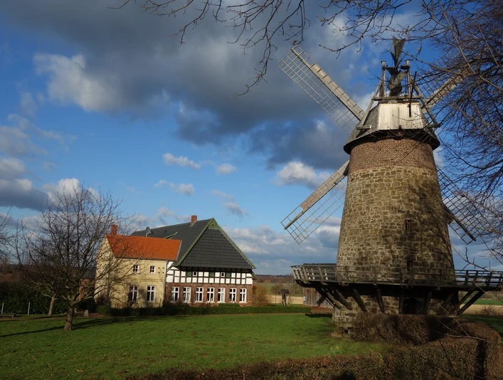 Historisches Mühlenensemble mit Backsteinturm und Fachwerkbau, umgeben von weitläufigen Wiesen.