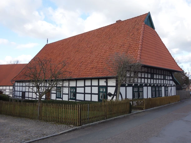 Gehrmker Hius Fachwerkhaus mit rotem Ziegeldach und weißen Wänden, umgeben von einem Holzzaun, bei bewölktem Himmel.