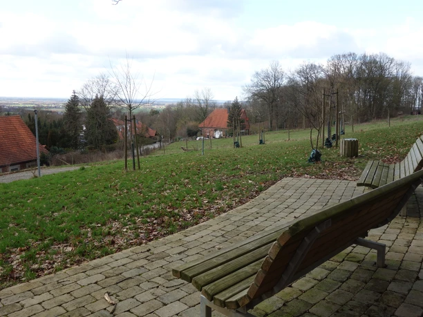Obermehnen-Aussicht Holzbänke auf einer gepflasterten Terrasse bieten einen weiten Blick über eine ländliche Landschaft.