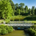 Preußisch Oldendorf-Kurensemble Bad Holzhausen-Teutoburger-Wald-Tourismus-D-Ketz-100.jpg Fußgängerbrücke über einen grünen Teich in einem üppigen Park mit Bäumen und Spaziergängern.