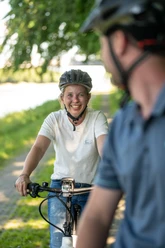 Preußisch Oldendorf-Mittellandkanal-Teutoburger-Wald-Tourismus-D-Ketz-094.jpg Zwei Radfahrer mit Helmen lächeln auf einem grünen Weg, der von Bäumen gesäumt ist, zueinander.