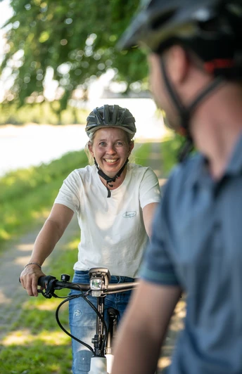 Preußisch Oldendorf-Mittellandkanal-Teutoburger-Wald-Tourismus-D-Ketz-094.jpg Zwei Radfahrer mit Helmen lächeln auf einem grünen Weg, der von Bäumen gesäumt ist, zueinander.
