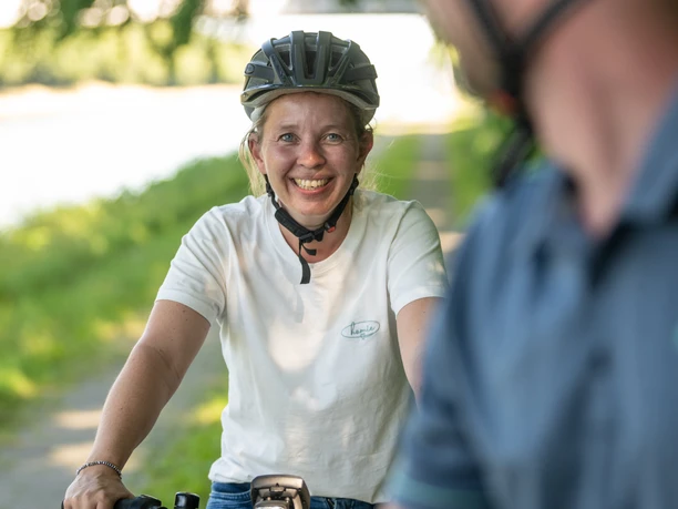 Preußisch Oldendorf-Mittellandkanal-Teutoburger-Wald-Tourismus-D-Ketz-094.jpg Zwei Radfahrer mit Helmen lächeln auf einem grünen Weg, der von Bäumen gesäumt ist, zueinander.