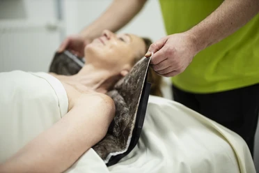 Moorpackung MEDICLIN Rose Klinik Eine Patientin erhält eine Moorpackung, betreut von einem Mitarbeiter in einem grünen Hemd.