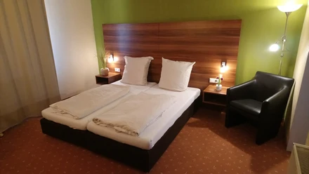DSC_2314.JPG Ein modernes Doppelzimmer mit grüner Akzentwand, zwei Einzelbetten, Nachttischlampen und einer Sitzgelegenheit.