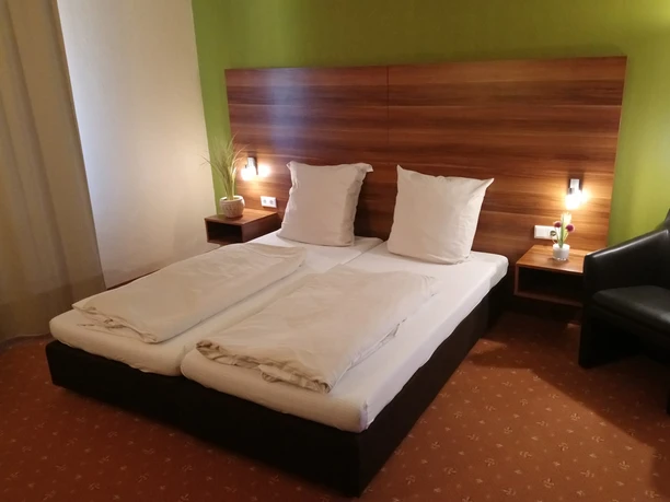 DSC_2314.JPG Ein modernes Doppelzimmer mit grüner Akzentwand, zwei Einzelbetten, Nachttischlampen und einer Sitzgelegenheit.