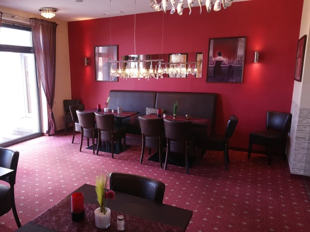 DSC_1971.JPG Ein eleganter Essbereich mit roten Wänden, hölzernen Tischen und Stühlen, dekoriert mit Kronleuchtern.