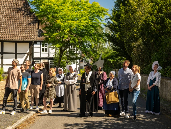 Stemwede-Stiftsort Levern-Teutoburger-Wald-Tourismus-D-Ketz-051.jpg Eine Gruppe Menschen in historischer Kleidung steht in einem sonnigen Dorf vor Fachwerkhäusern.