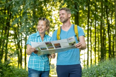 Stemwede-Waldlehrpfad Stemweder Berg-Teutoburger-Wald-Tourismus-D-Ketz-035.jpg Zwei fröhliche Wanderer mit Karte auf einem bewaldeten Lehrpfad im Sonnenlicht.