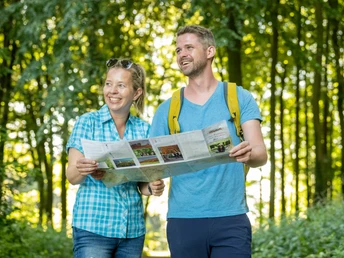 Stemwede-Waldlehrpfad Stemweder Berg-Teutoburger-Wald-Tourismus-D-Ketz-035.jpg Zwei fröhliche Wanderer mit Karte auf einem bewaldeten Lehrpfad im Sonnenlicht.