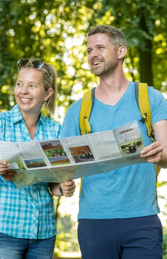 Stemwede-Waldlehrpfad Stemweder Berg-Teutoburger-Wald-Tourismus-D-Ketz-035.jpg Zwei fröhliche Wanderer mit Karte auf einem bewaldeten Lehrpfad im Sonnenlicht.