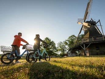 Stemwede-Mühlenensemble Levern-Teutoburger-Wald-Tourismus-D-Ketz-012.jpg Zwei Personen auf Fahrrädern blicken bei Sonnenuntergang auf eine historische Windmühle.