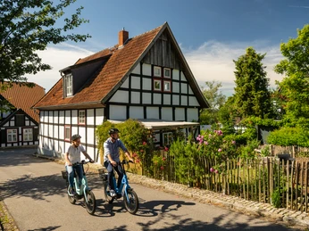 Stemwede-Stiftsort Levern-Teutoburger-Wald-Tourismus-D-Ketz-047.jpg Zwei Personen radeln auf gemieteten E-Bikes vor einem traditionellen Fachwerkhaus in Stemwede-Levern.
