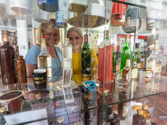 Zwei Frauen betrachten Flaschen in einem Regal, umgeben von verschiedenen Spirituosen in einer Ausstellung.