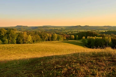 Gossdorf Hankehübel Uitzicht Uitgestrekt landschap met glooiende heuvels en bossen in het gouden licht van de zonsondergang, de lucht is helder en licht oranje van kleur.