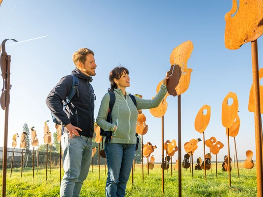 Nieheim-Nieheimer Kunstpfad Holzhausen-Teutoburger-Wald-Tourismus-D-Ketz-003.jpg Mann und Frau stehen auf einer Wiese, umgeben von Metallskulpturen, bei klarem Himmel.