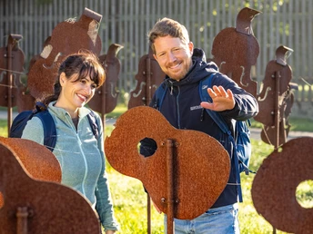 Nieheim-Nieheimer Kunstpfad Holzhausen-Teutoburger-Wald-Tourismus-D-Ketz-004.jpg Zwei lächelnde Personen interagieren mit rostigen Gitarren-Skulpturen auf einer sonnigen Wiese.