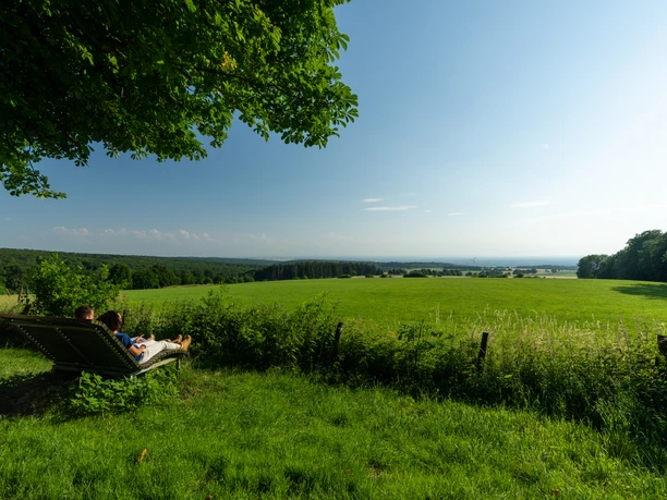 Schlangen-Bauerkamp-Teutoburger-Wald-Tourismus-Patrick-Gawandtka-100-CC-BY-SA.jpg Menschen genießen auf einer Wiese liegend den Panoramablick über eine grüne Landschaft unter blauem Himmel.