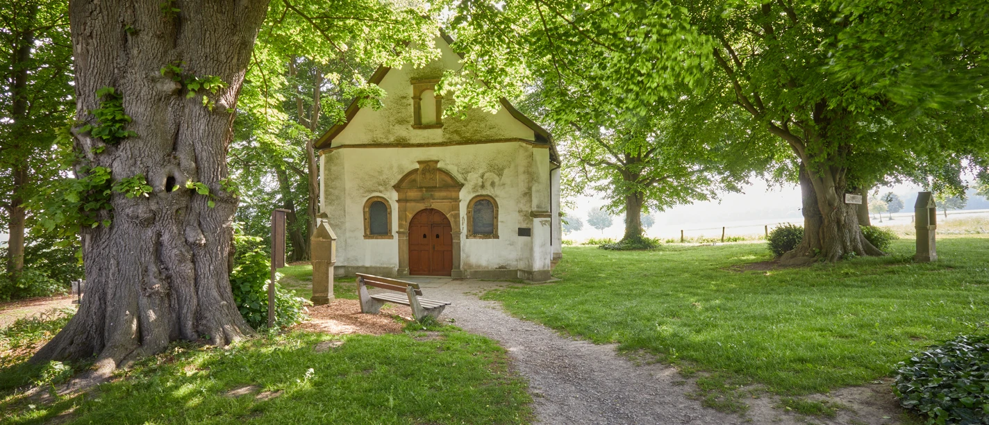 Eine idyllische Kapelle, umgeben von alten Bäumen und saftigem Grün, mit einem einladenden Pfad.