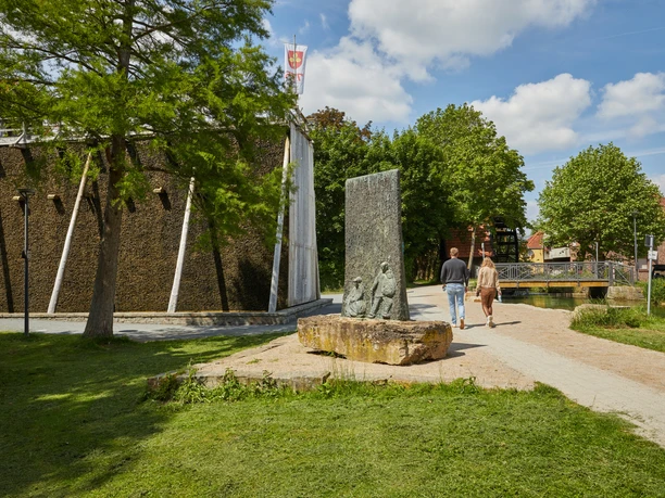Paar spaziert bei sonnigem Wetter entlang eines barrierefreien Wegs an einem modernen Gebäude vorbei.