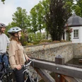 Borchen-Mallinckrodthof-Teutoburger-Wald-Tourismus-T-Evers-138.jpg Zwei Personen mit Fahrrädern stehen auf einer Holzbrücke und blicken auf ein malerisches Wasserschloss.