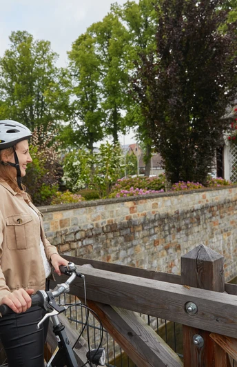 Borchen-Mallinckrodthof-Teutoburger-Wald-Tourismus-T-Evers-138.jpg Zwei Personen mit Fahrrädern stehen auf einer Holzbrücke und blicken auf ein malerisches Wasserschloss.