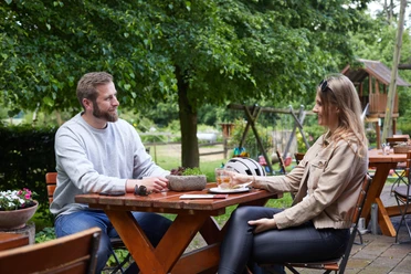 Borchen-Kapellenhof-Teutoburger-Wald-Tourismus-T-Evers-096.jpg Zwei Personen sitzen an einem Holztisch im Freien; im Hintergrund grüner Garten mit Spielgeräten.