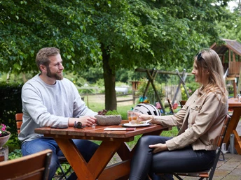 Borchen-Kapellenhof-Teutoburger-Wald-Tourismus-T-Evers-096.jpg Zwei Personen sitzen an einem Holztisch im Freien; im Hintergrund grüner Garten mit Spielgeräten.