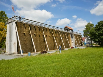 Salzkotten-Saline-Teutoburger-Wald-Tourismus-T-Evers-054.jpg Ein Gradierwerk im Grünen; Besucher spazieren auf dem Weg daneben. Holzgerüst mit Reisig, klarer Himmel.