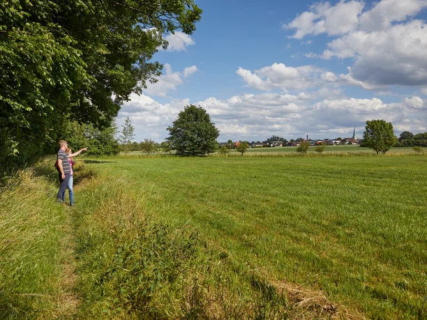 Langenberg-Forthbachweg-Teutoburger-Wald-Tourismus-T-Evers-007.jpg Ein Wanderer zeigt auf eine weite, grüne Wiese unter blauem Himmel mit vereinzelten Bäumen.