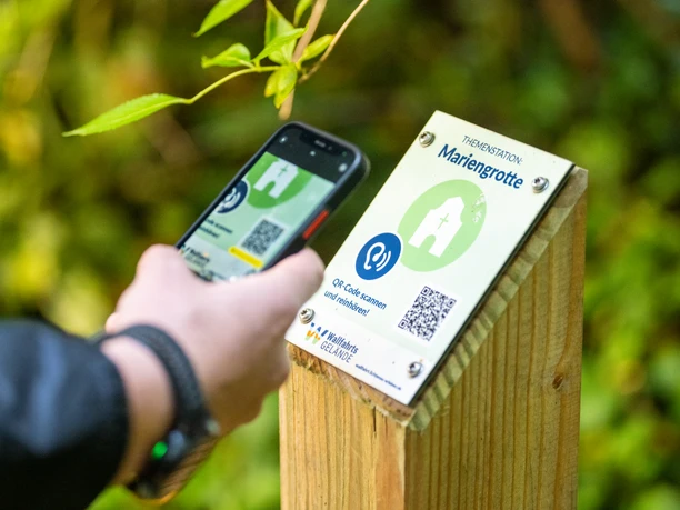 Eine Person scannt einen QR-Code an einem Schild mit der Aufschrift "Mariengrotte".