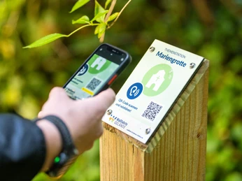 Lichtenau-Wallfahrtsgelände Kleinenberg-Teutoburger-Wald-Tourismus-D-Ketz-054.jpg Eine Person scannt einen QR-Code an einem Schild mit der Aufschrift "Mariengrotte".