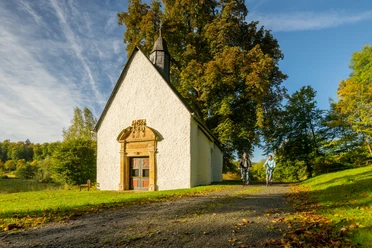 Lichtenau-Annenkapelle-Teutoburger-Wald-Tourismus-D-Ketz-009.jpg Zwei Radfahrer passieren eine kleine, weiße Kapelle in einer herbstlichen Landschaft bei sonnigem Wetter.