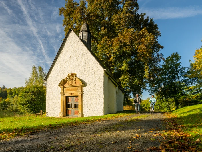 Lichtenau-Annenkapelle-Teutoburger-Wald-Tourismus-D-Ketz-009.jpg Zwei Radfahrer passieren eine kleine, weiße Kapelle in einer herbstlichen Landschaft bei sonnigem Wetter.