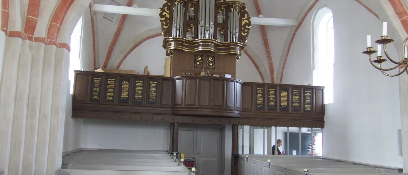 Kirche mit Orgel in Canum Innenraum der Kirche Canum mit gotischem Gewölbe, grauen Bänken und der Orgel auf der Empore.