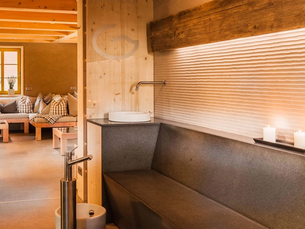 Cozy room with wooden ceiling, gray sofa, candles and a modern faucet over a white sink; warm, inviting atmosphere.