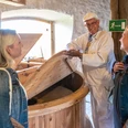 Drei Personen in traditioneller Kleidung stehen in einer historischen Mühle, umgeben von Holzelementen.