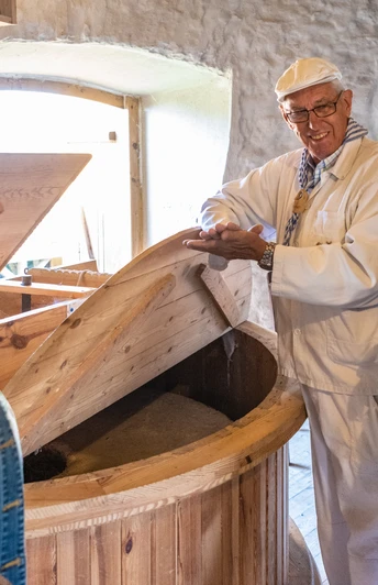 Porta Westfalica-Windmühle Holzhausen-Teutoburger-Wald-Tourismus-D-Ketz-027.jpg Drei Personen in traditioneller Kleidung stehen in einer historischen Mühle, umgeben von Holzelementen.