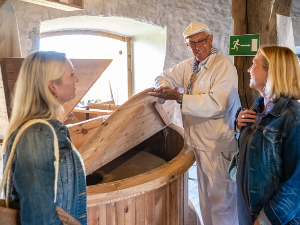 Porta Westfalica-Windmühle Holzhausen-Teutoburger-Wald-Tourismus-D-Ketz-027.jpg Drei Personen in traditioneller Kleidung stehen in einer historischen Mühle, umgeben von Holzelementen.