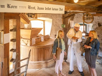 Porta Westfalica-Windmühle Holzhausen-Teutoburger-Wald-Tourismus-D-Ketz-032.jpg Eine historische Getreidemühle, in der ein Müller zwei Besucherinnen die Kunst des Mahlens erklärt.