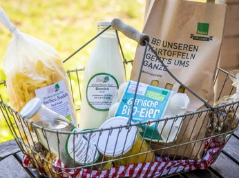 Ein Metallkorb voll regionaler Produkte: Eier, Milch, Pasta, Brot und eine Tüte vom Biohof.