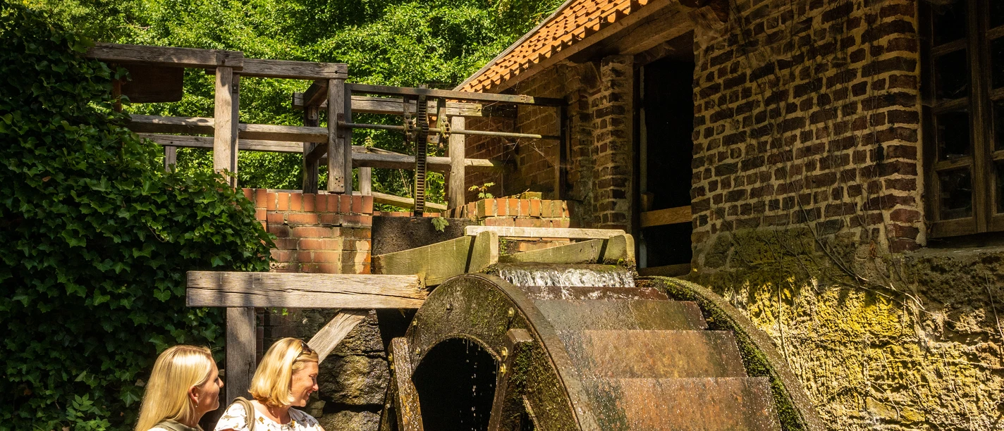 Bad-Oeynhausen-Wassermühle Bergkirchen Holzhausen-Teutoburger-Wald-Tourismus-D-Ketz-057.jpg Zwei Frauen stehen draußen vor dem Mühlrad der Wassermühle Bergkirchen in Bad Oeynhausen