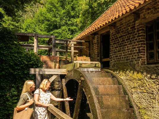 Bad-Oeynhausen-Wassermühle Bergkirchen Holzhausen-Teutoburger-Wald-Tourismus-D-Ketz-057.jpg Zwei Frauen stehen draußen vor dem Mühlrad der Wassermühle Bergkirchen in Bad Oeynhausen