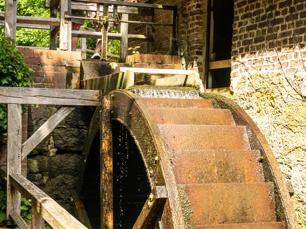 Zwei Frauen stehen oberhalb des Mühlrads der Wassermühle Bergkirchen in Bad Oeynhausen und schauen auf das Mühlrad